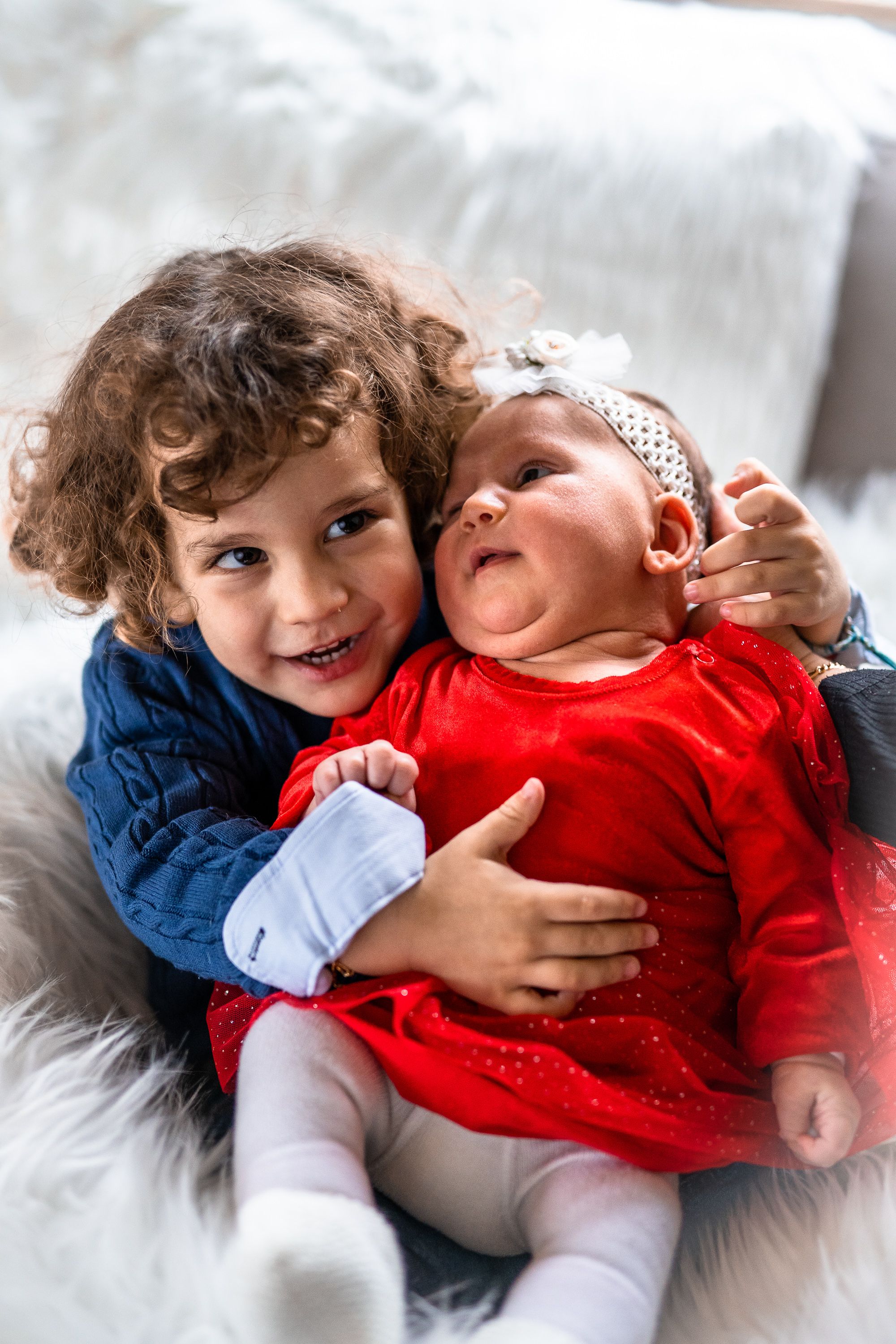 Two young children cuddling on white fur blanket with holiday outfits.