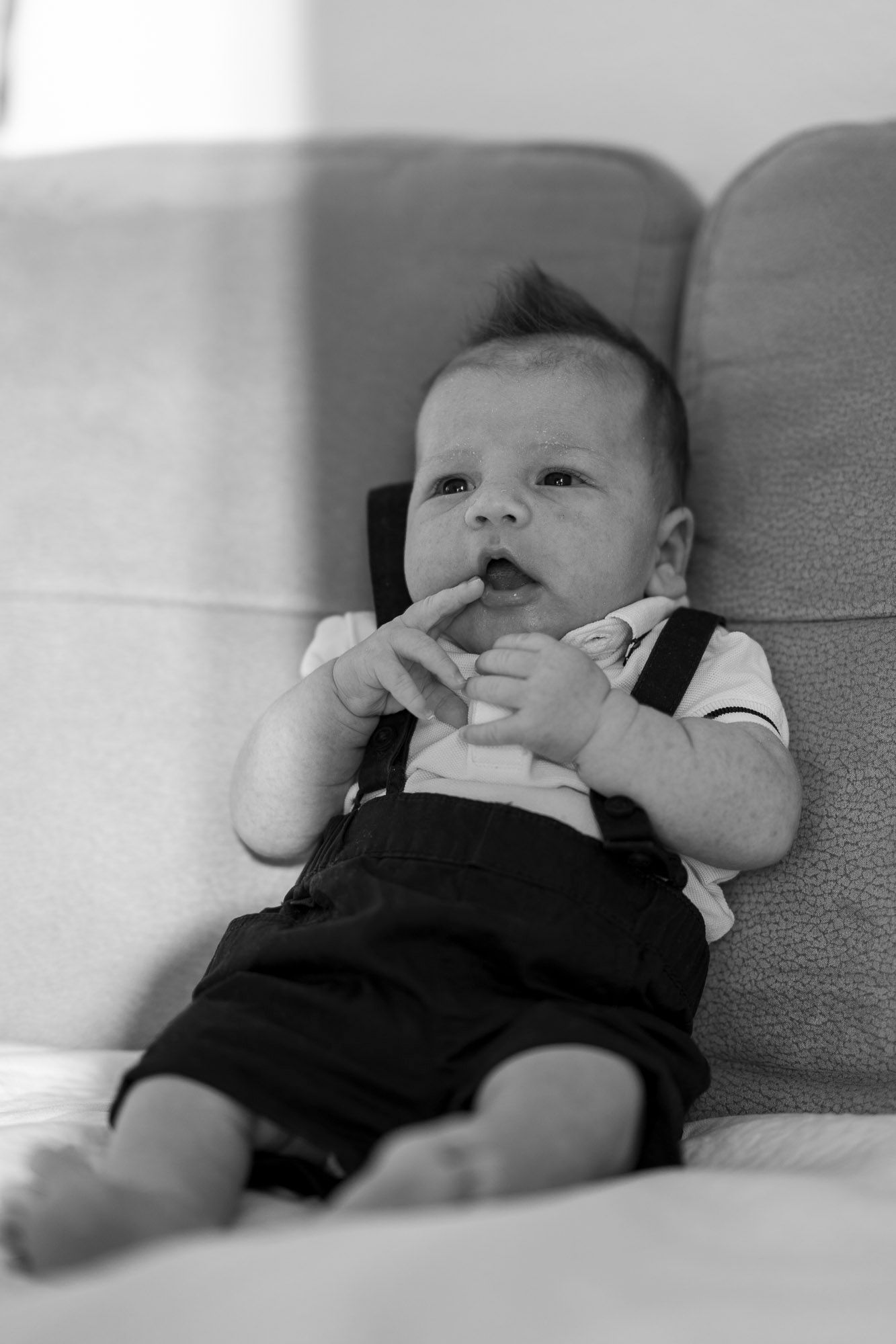 Baby in black and white wearing overalls laying on couch.