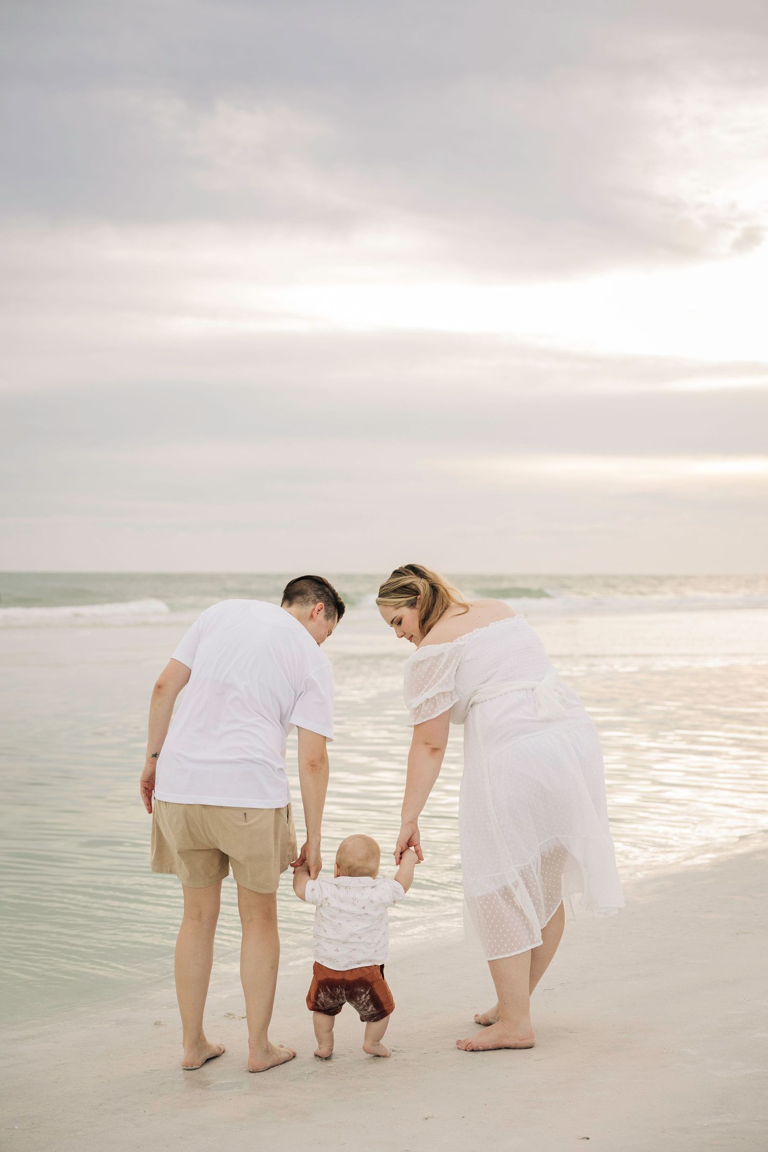 Lesbian couple family holding hands with baby on Siesta Key Beach taken by Siesta Key Family Photographer.
