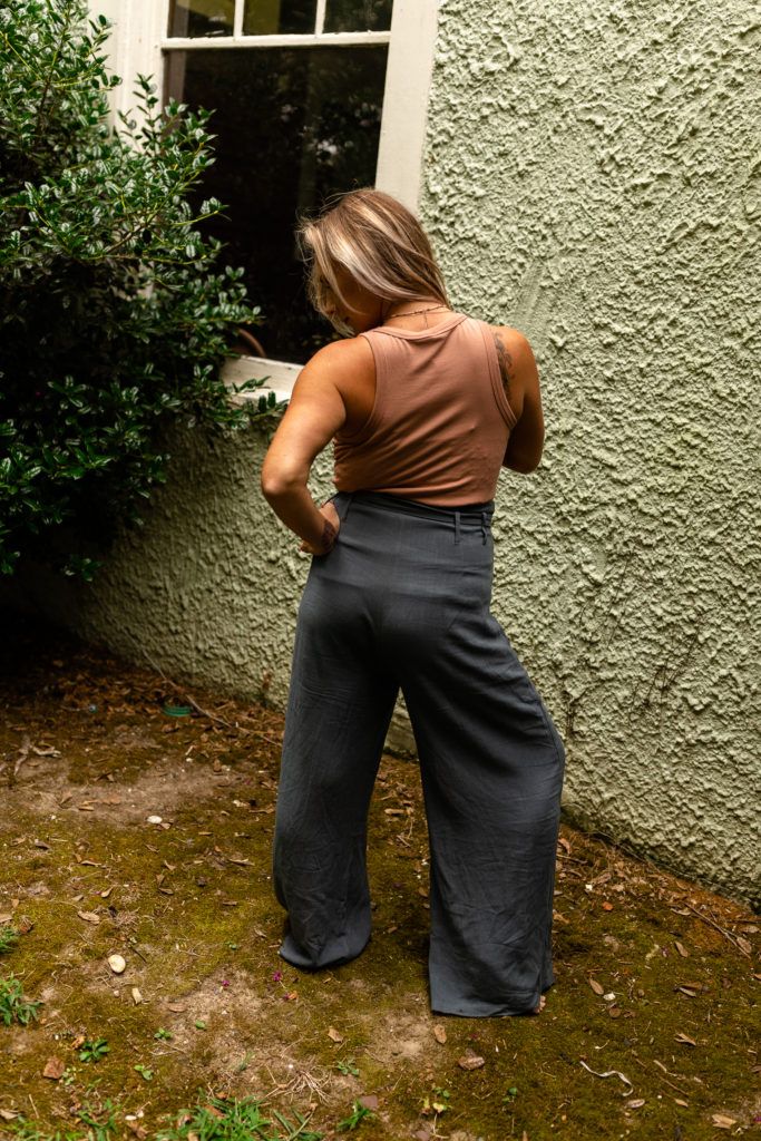 Back view of person wearing brown tank top and wide-leg gray pants standing near wall.