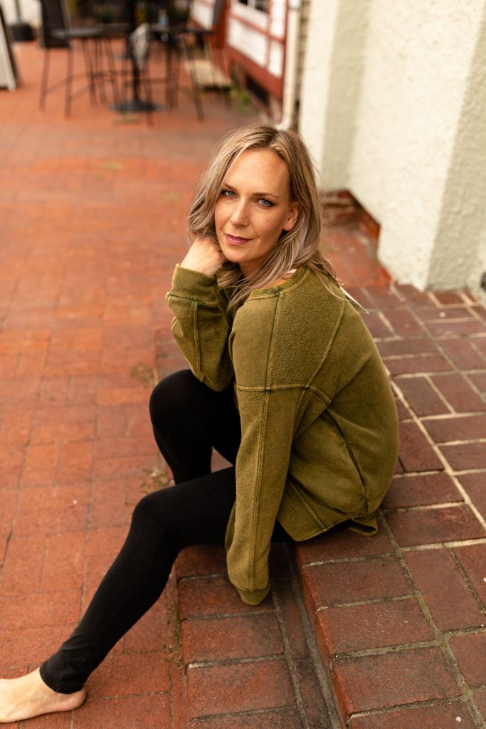 Casual portrait of woman in olive green sweater sitting on brick steps.