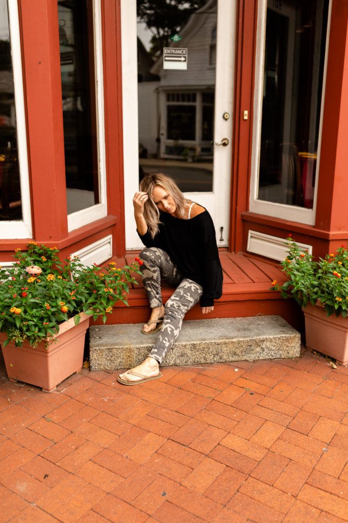 Woman in black sweater and patterned leggings sitting on red-trimmed storefront steps.
