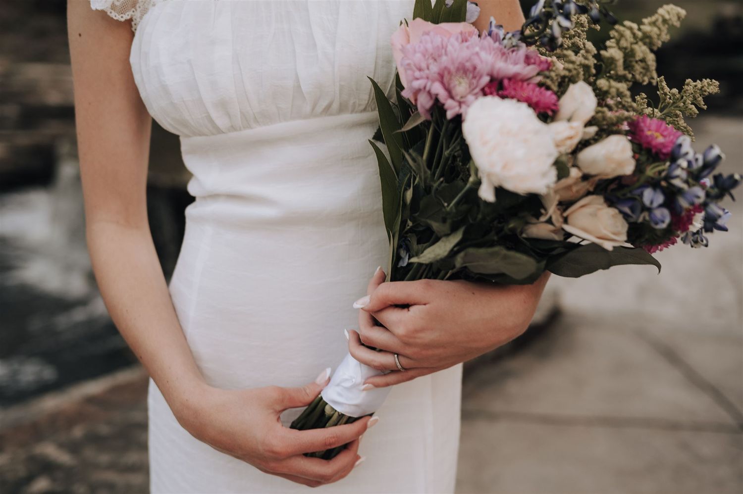 Detail shot of white dress with delicate lace sleeves holding a pink and white floral bouquet.