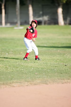Youth baseball player in red uniform positions to field ground ball.