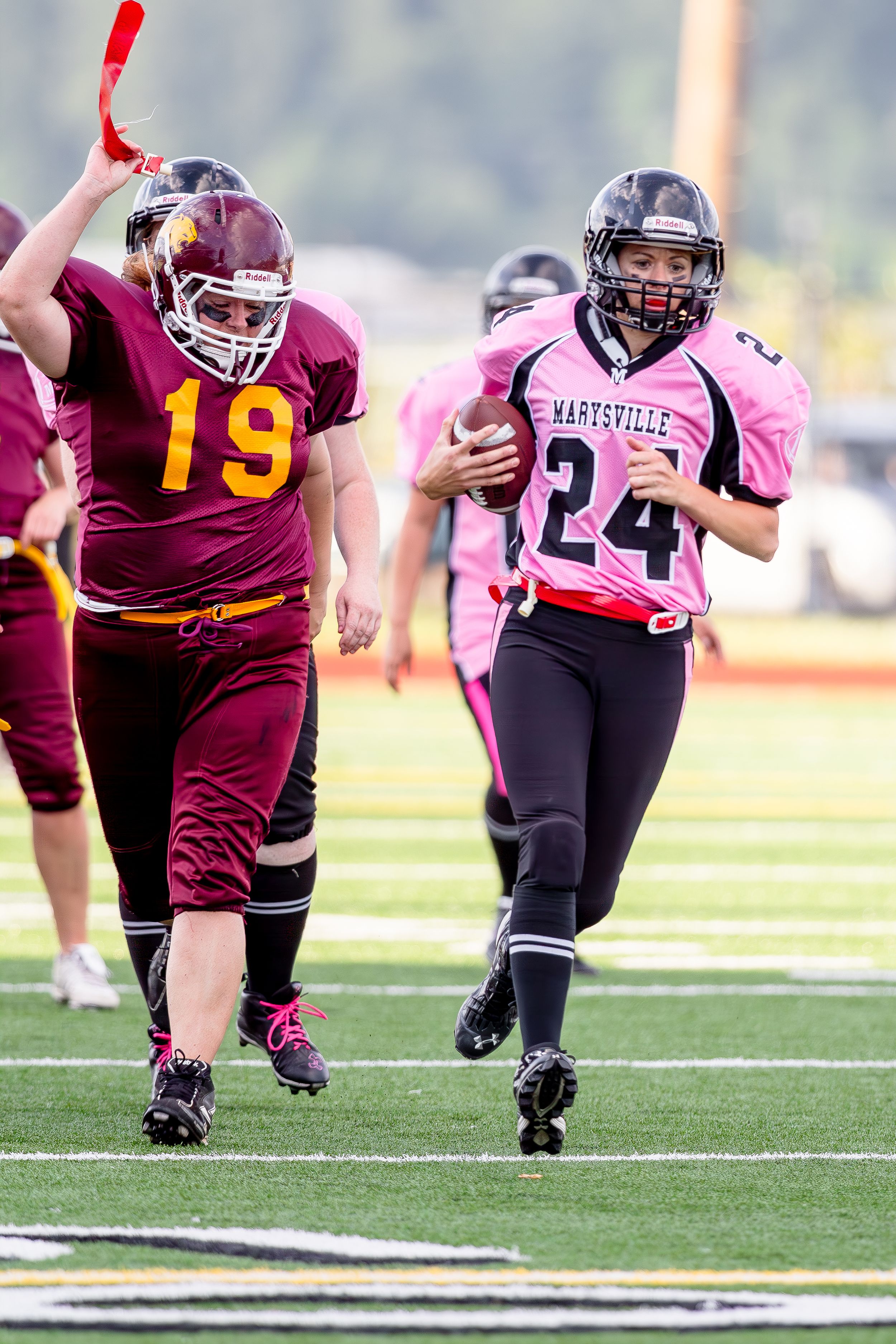 Football action shot with players in maroon and pink jerseys running on the field.