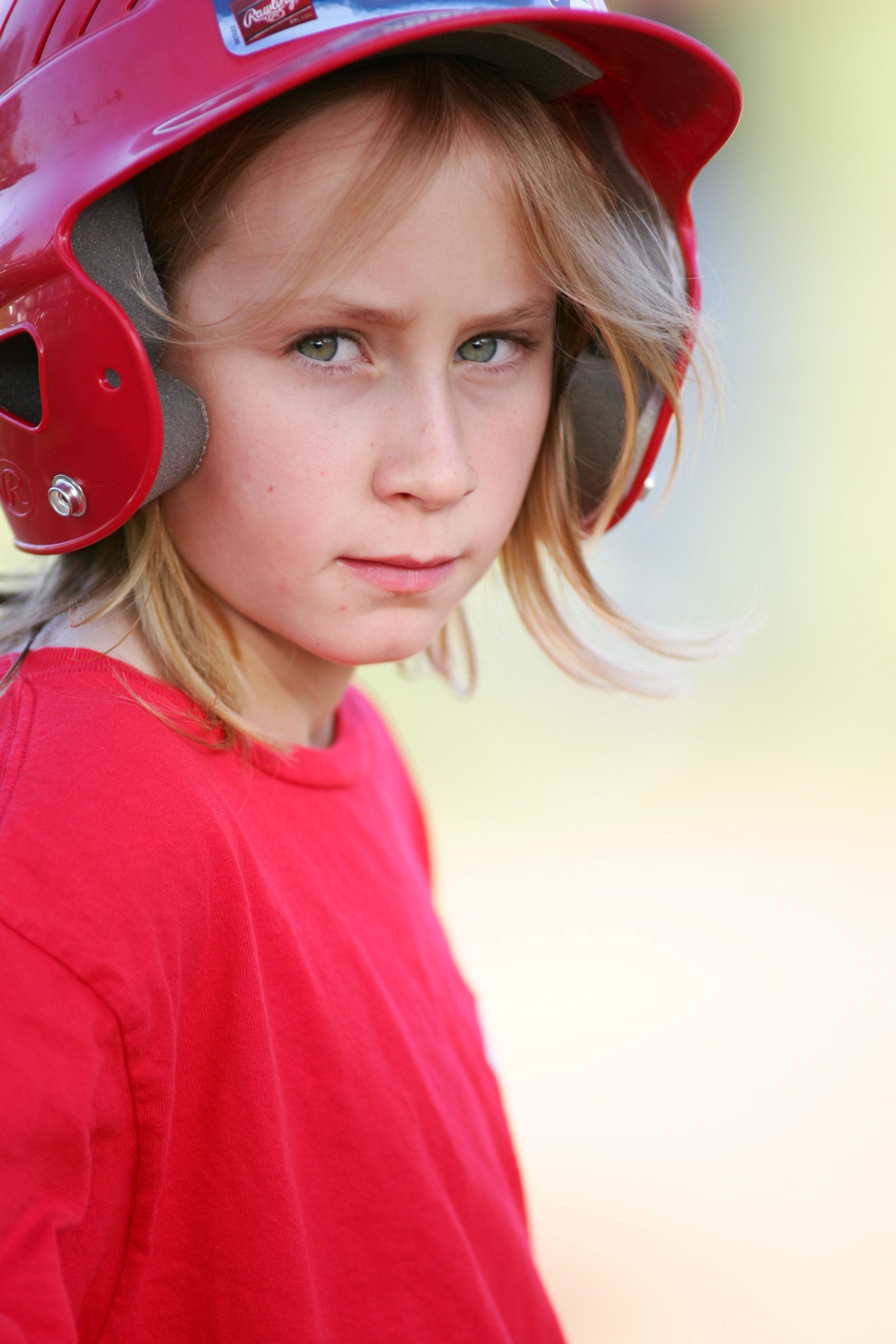 young boy in a red shirt and baseball helmet looks at the camera