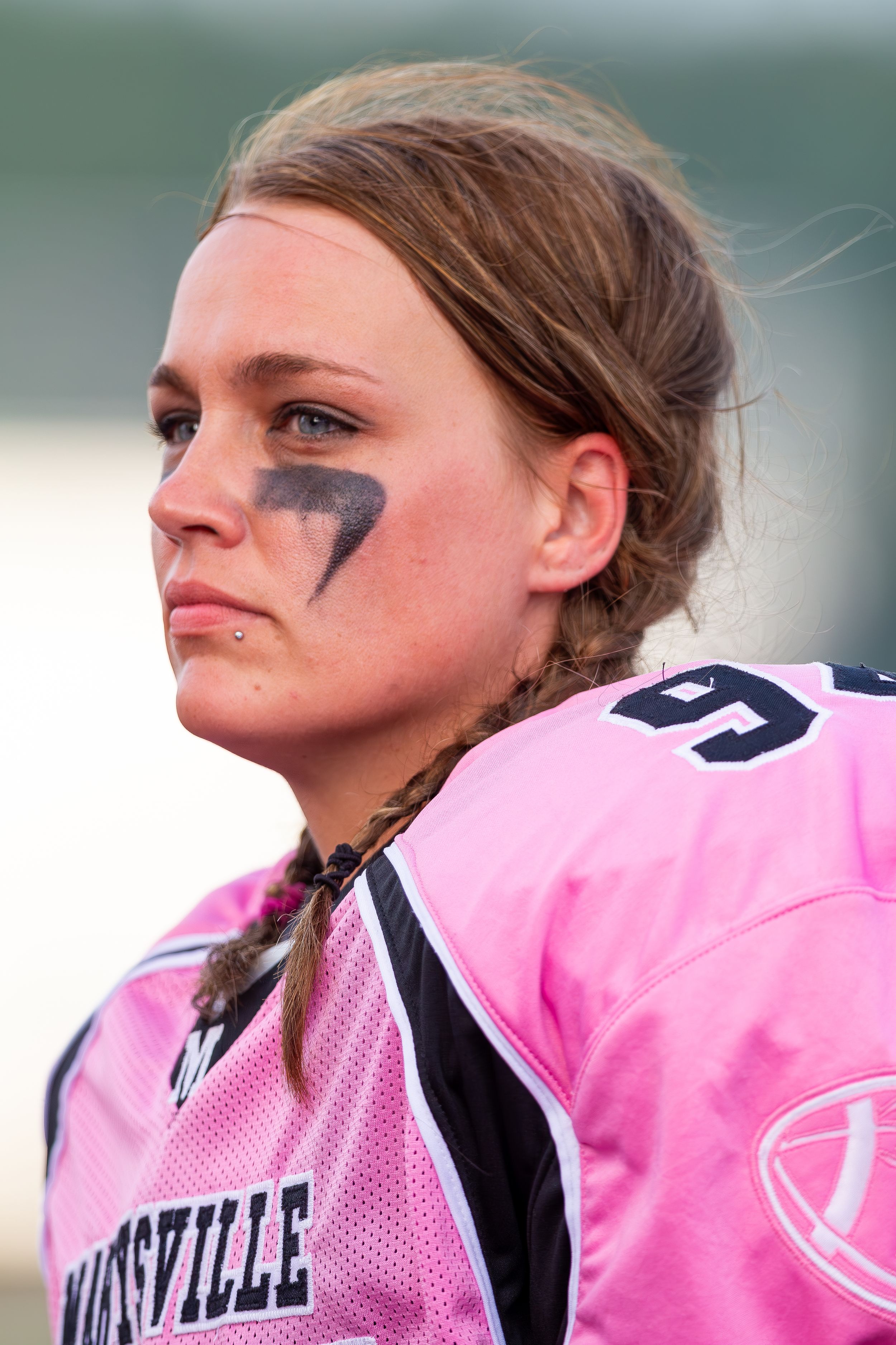 Close-up of athlete in pink jersey with face paint and braided hair.