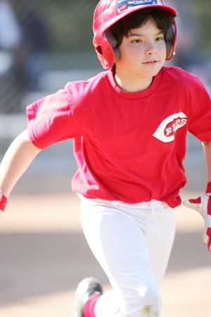Youth baseball player in red jersey running on baseball field.
