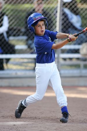 Young baseball player in blue and white uniform swings bat during youth baseball game on dirt field.