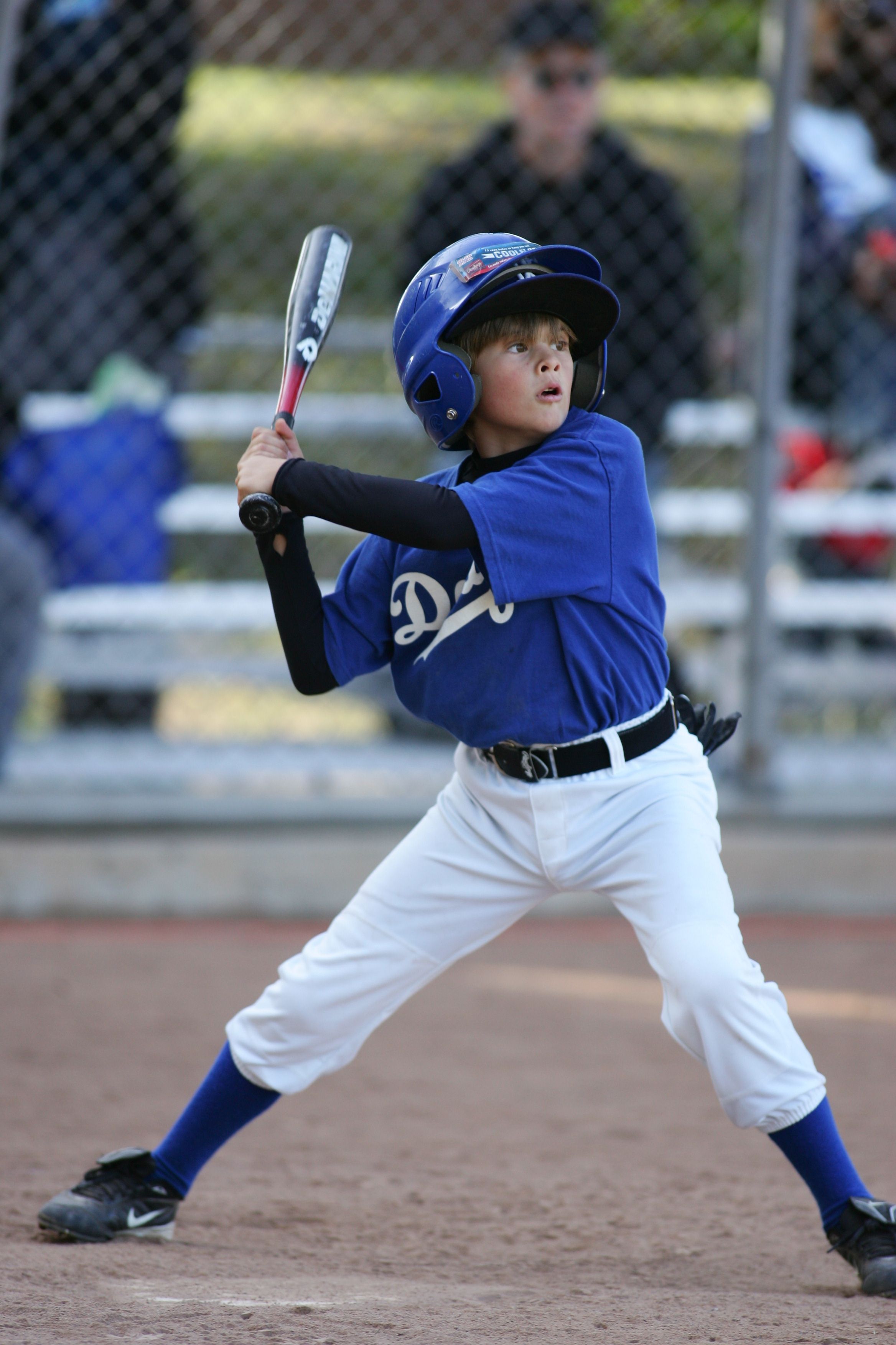 Little League player in Dodgers uniform takes batting stance at home plate.