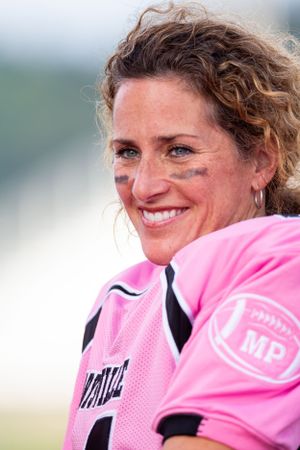 Football player wearing pink jersey with black face paint smiling during a game.