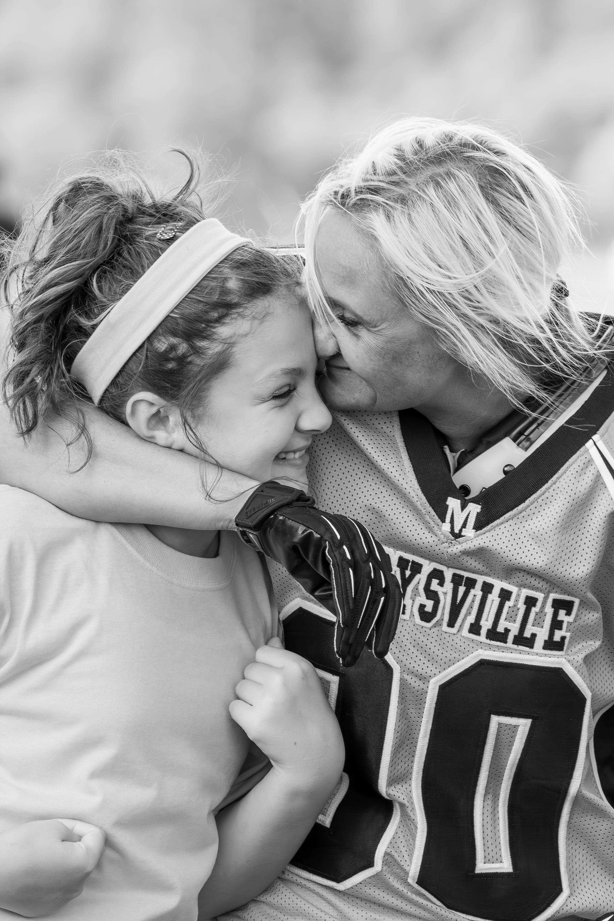 mom in football gear embraces and kisses her young daughter in celebration