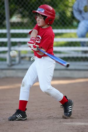 Youth baseball player in red uniform swings bat during baseball game.