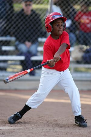 Little League player in red uniform swings baseball bat during game.