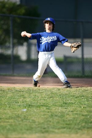 Youth baseball player in Dodgers uniform throws ball during game on grass field.