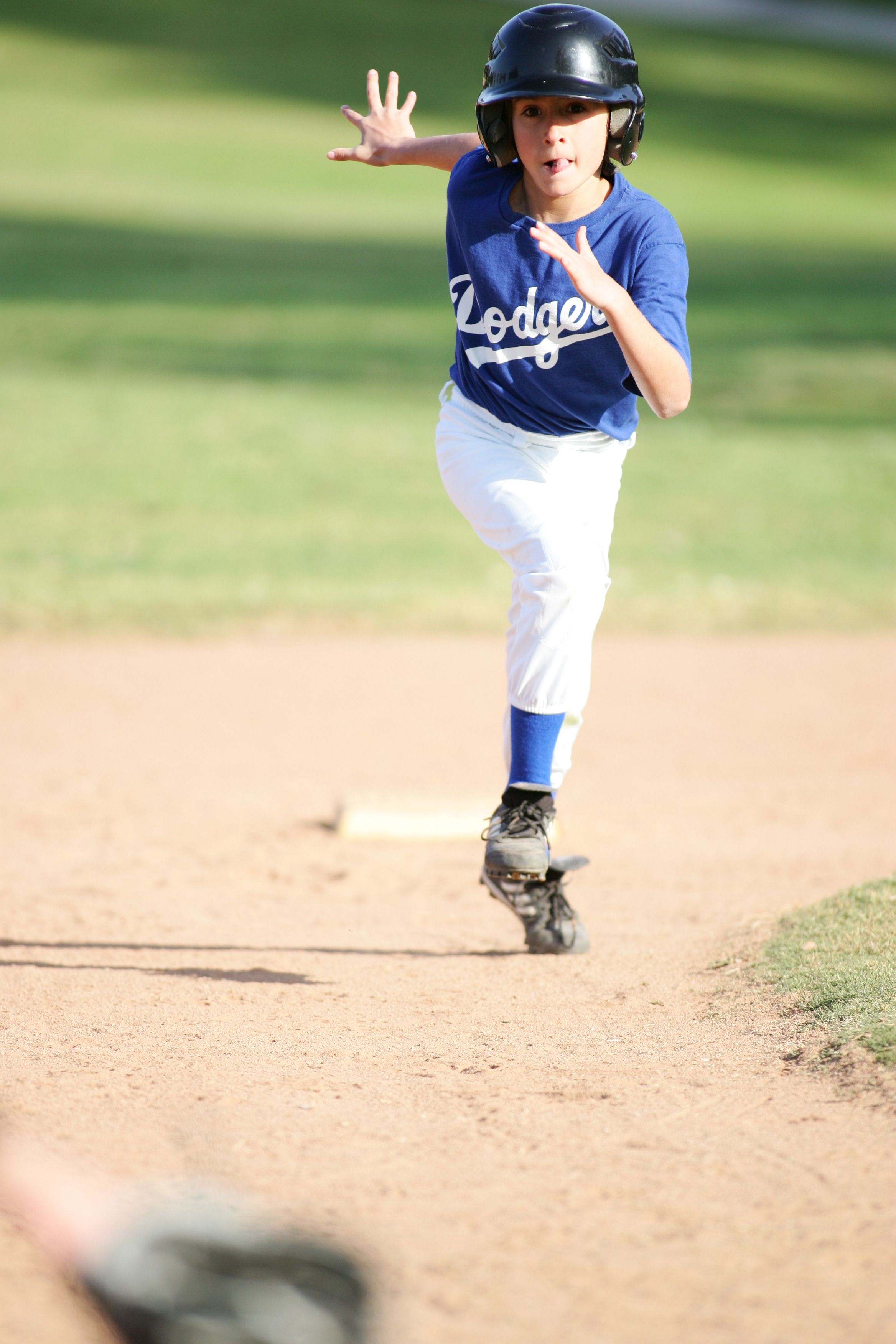 Baseball player in Dodgers uniform runs bases during youth league game.