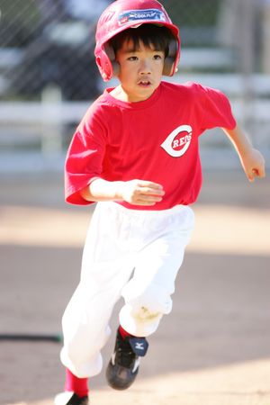 Young baseball player in red Reds uniform running on field.