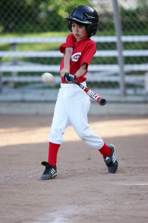 Youth baseball player in red jersey swings bat during game on dirt field.