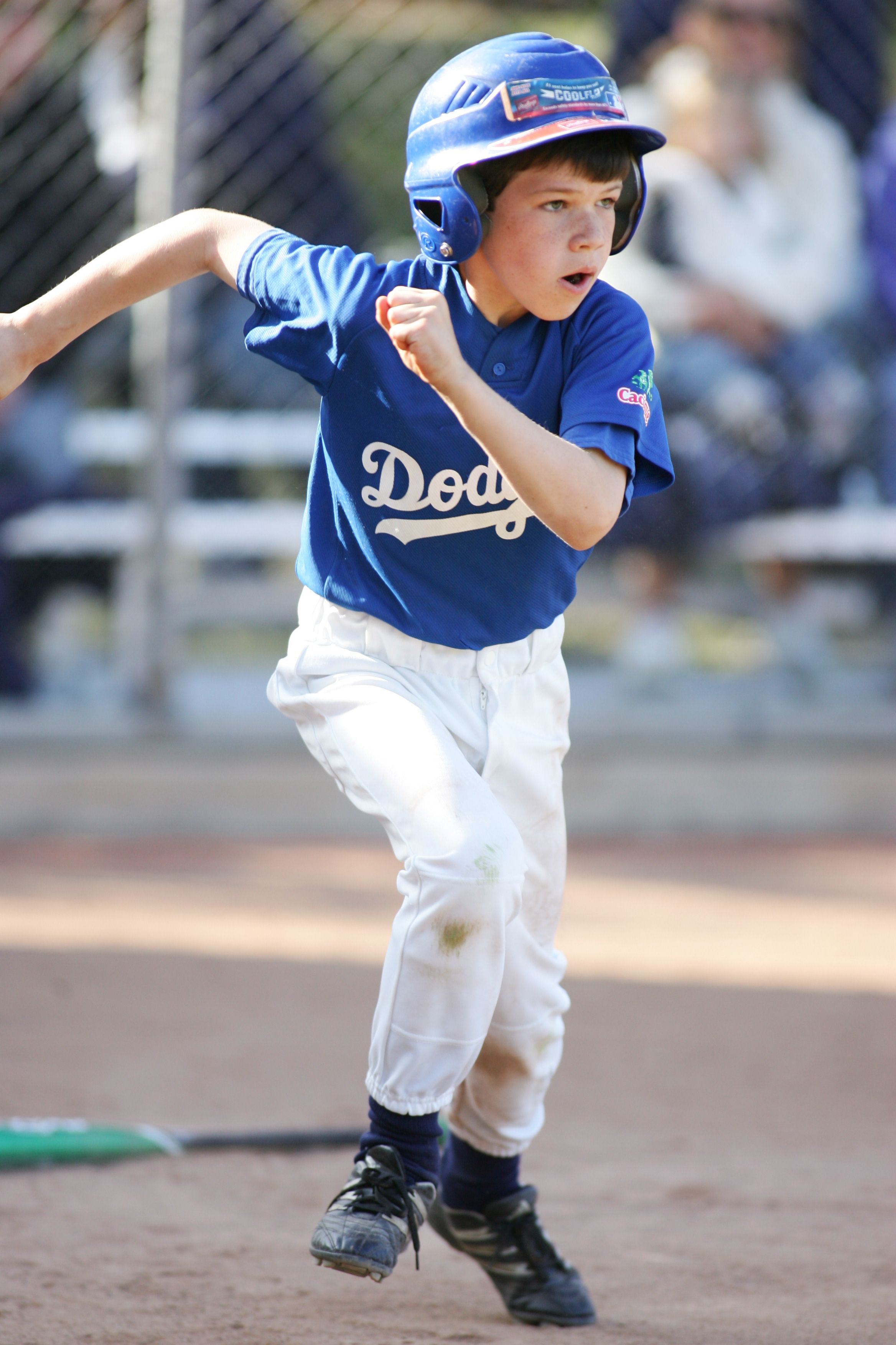 Youth baseball player in Dodgers uniform running bases during game.
