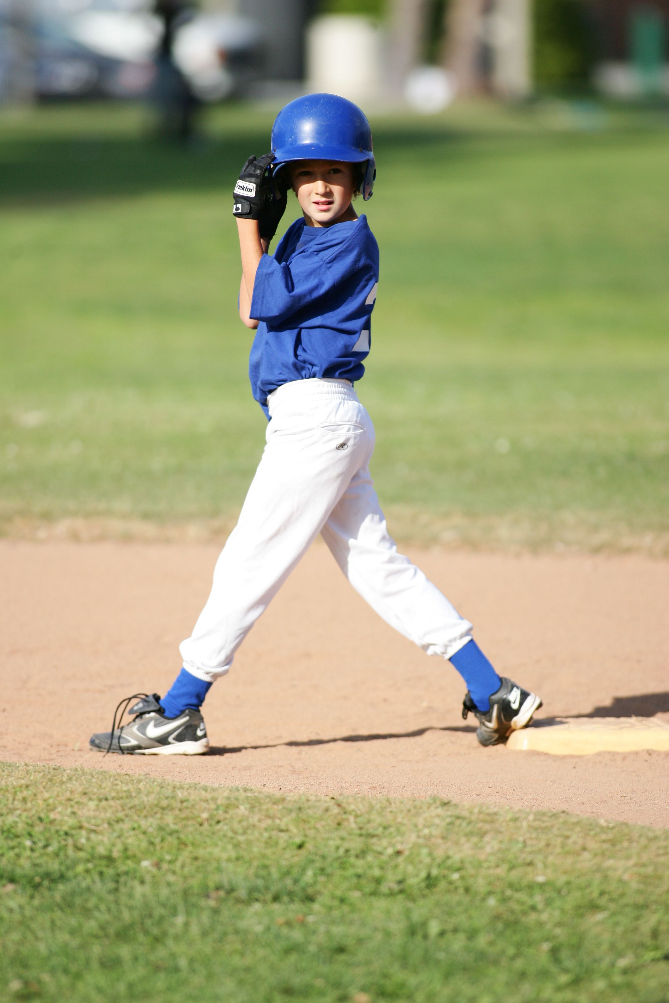 Young baseball player in blue uniform practices batting stance on sunny baseball field.