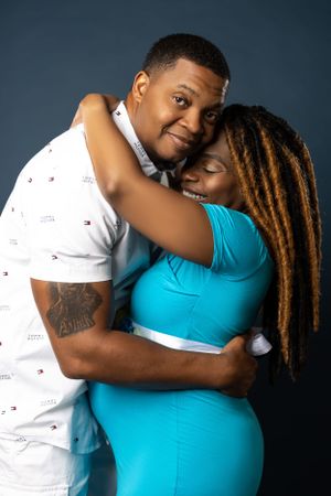 A tender embrace captured during a maternity photoshoot against dark background.