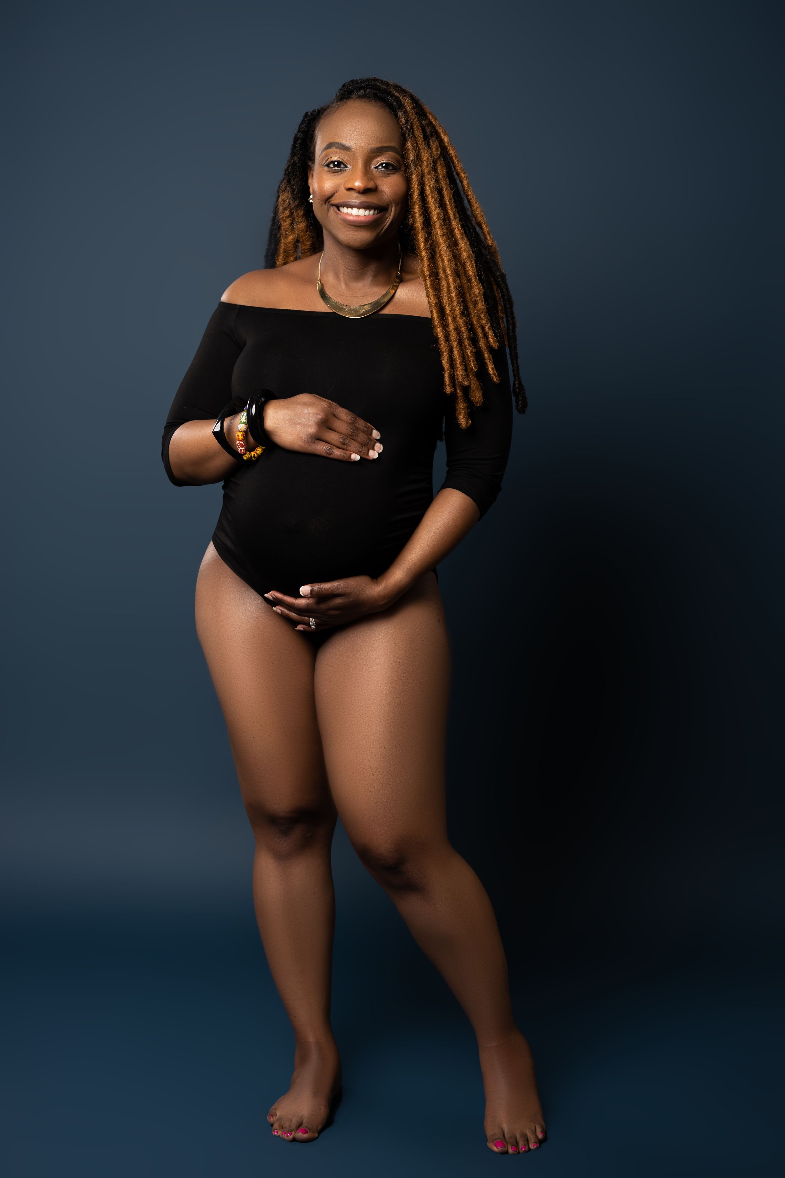 An artistic maternity portrait showcasing a black bodysuit and natural hair.