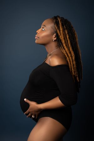 A side-profile maternity portrait against a dark blue background.