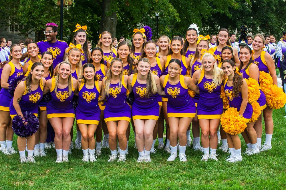 Large group of cheerleaders in purple uniforms posing together on a green lawn.