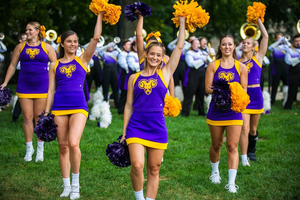 College cheerleaders in purple and gold uniforms performing at an outdoor pep rally.