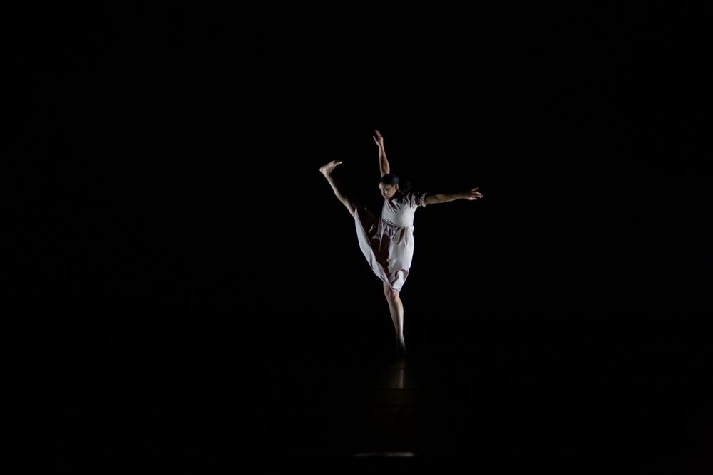 Solo dancer performs an expressive contemporary dance routine against a dark black background.
