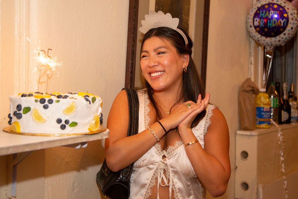 Young woman smiling and clapping at her birthday party, holding a decorated cake with sparklers.