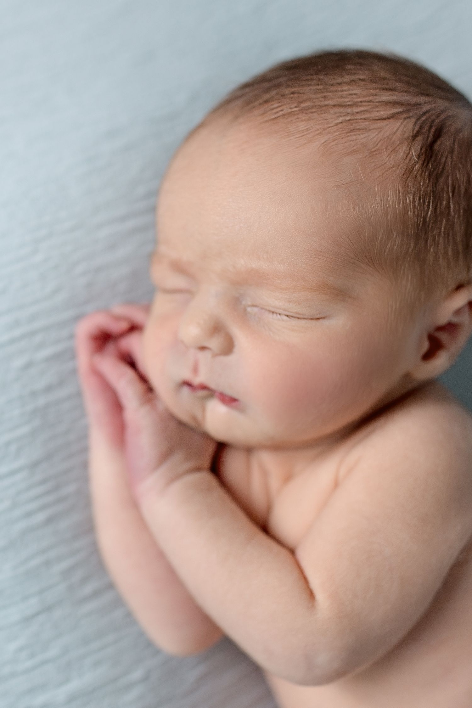 Newborn baby sleeping peacefully on light blue textured background.