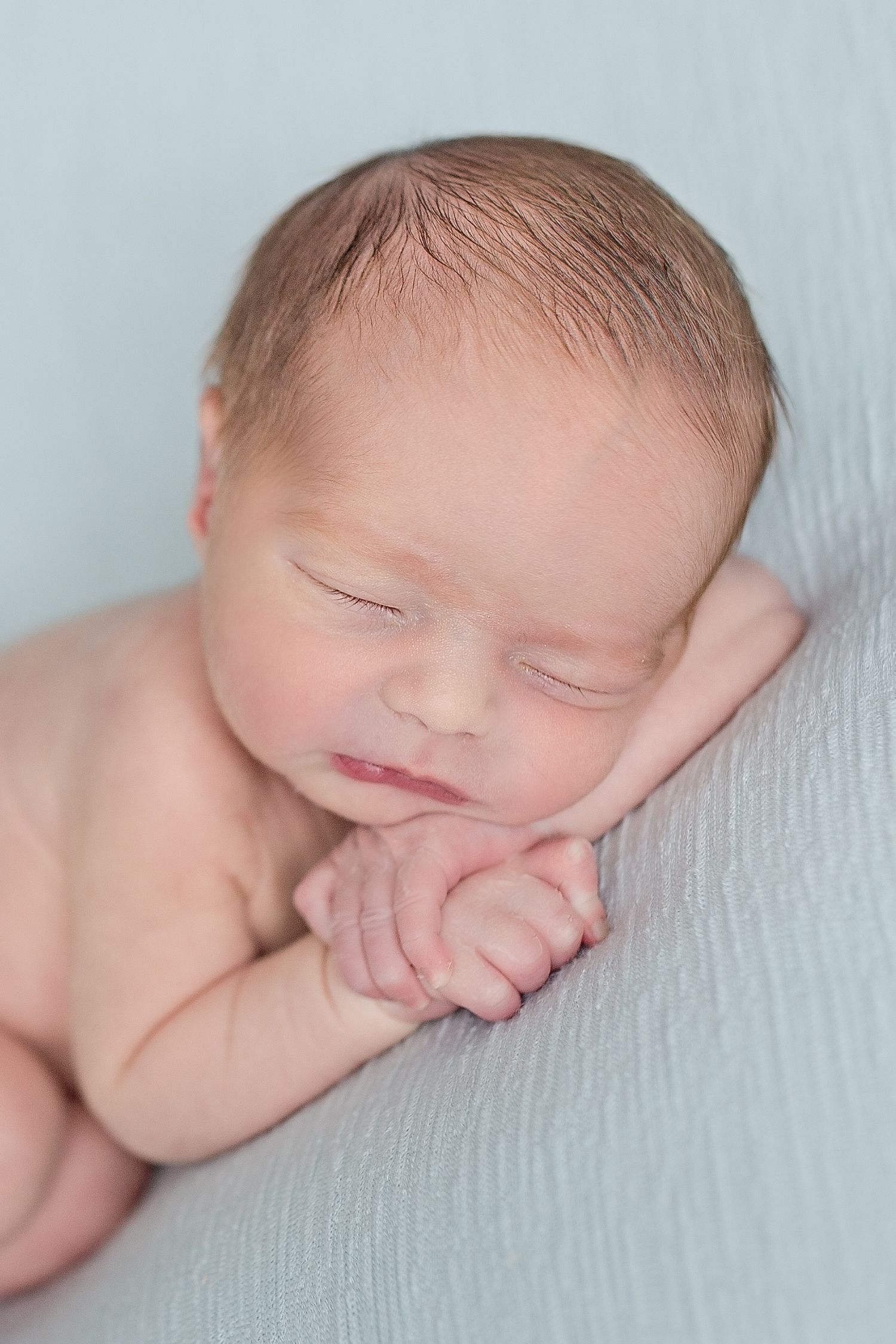 Peaceful sleeping newborn baby resting on soft blue blanket in natural light.