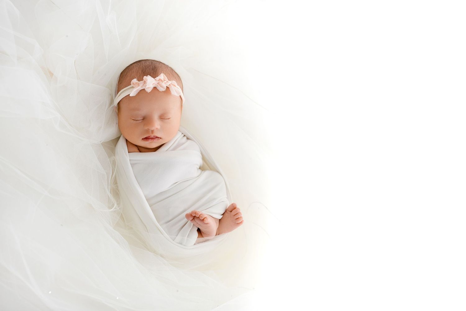 Peaceful sleeping newborn wrapped in white swaddle with delicate headband.
