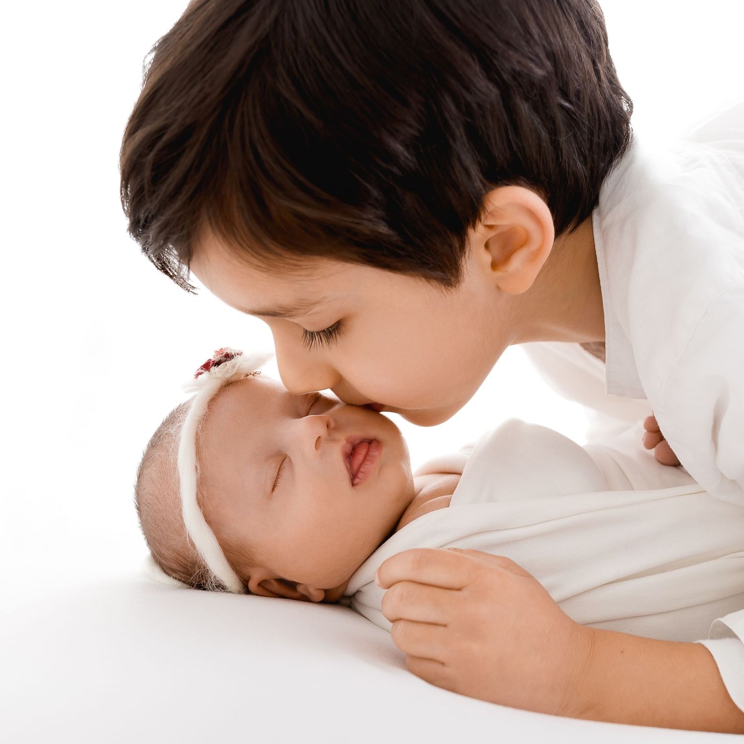 Sweet sibling moment with gentle kiss shared between baby and older child.
