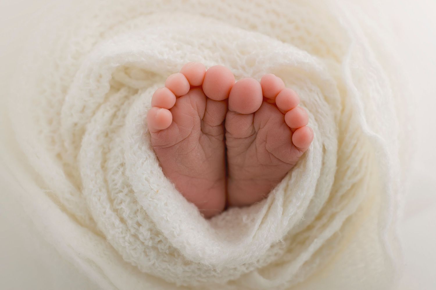 Close-up of tiny newborn feet nestled in soft white fabric.