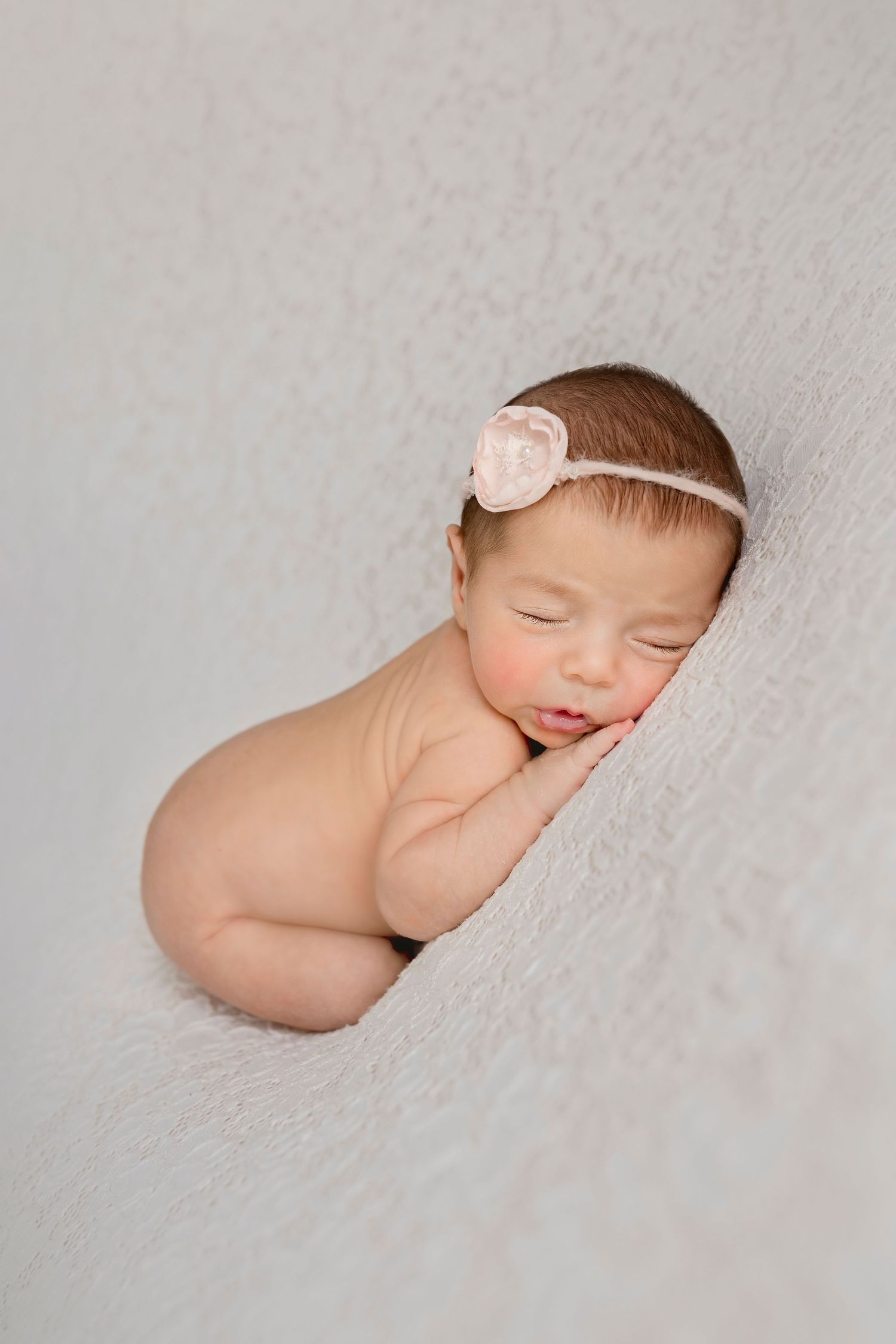 Artistic newborn portrait with pink headband against textured background.