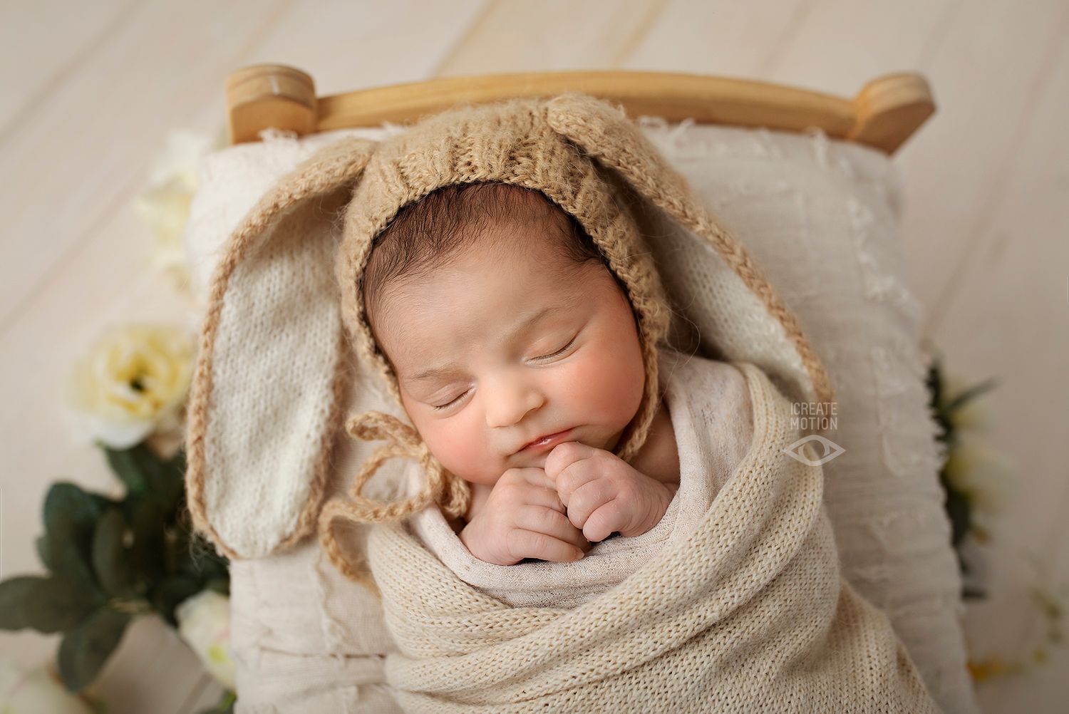 Sleeping newborn wearing cozy bunny ear hat nestled in cream blanket.