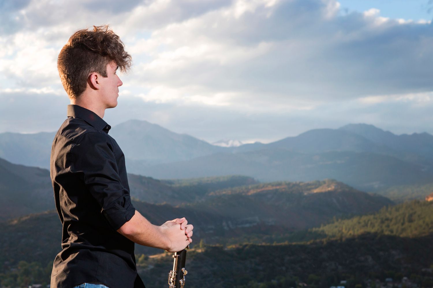 Musician with instrument looking out over scenic mountain landscape at dusk.