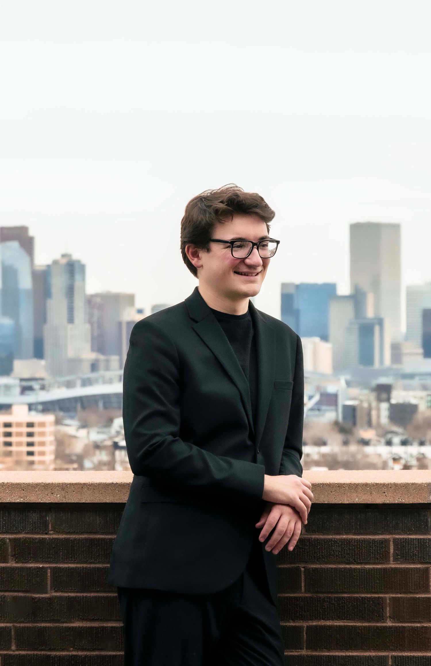 A man stands in front of the Denver skyline and smiles during a portrait session