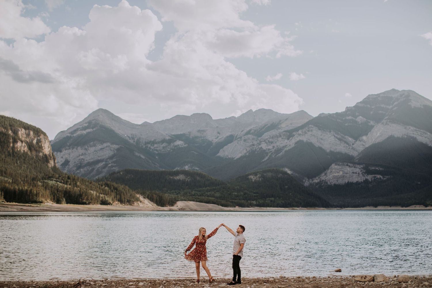 Two figures share a joyful moment by a scenic mountain lake.