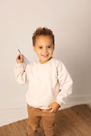 Young child wearing a light pink sweater and brown pants smiles while standing on a textured rug. Kendall Kuss Photography baby photos at st