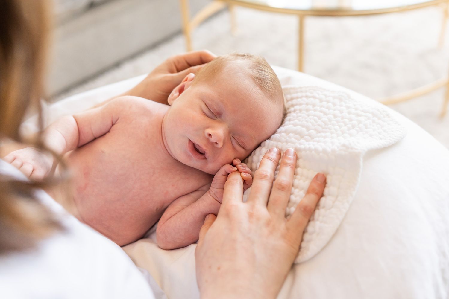 Baby girl holding onto mom's fingers at an in home newborn photo session.