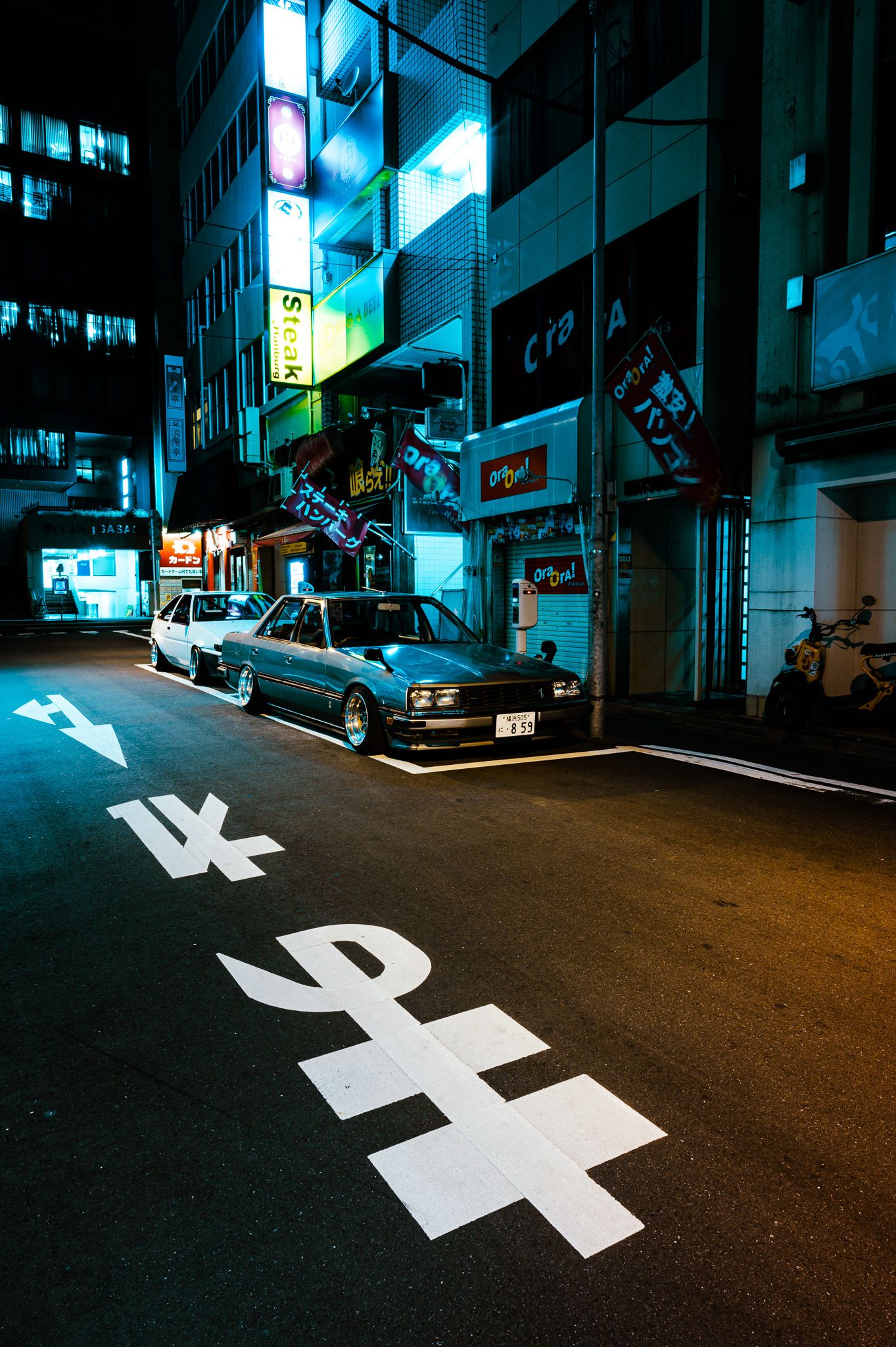 Vintage sedan parked on dark street with Japanese characters painted on asphalt.