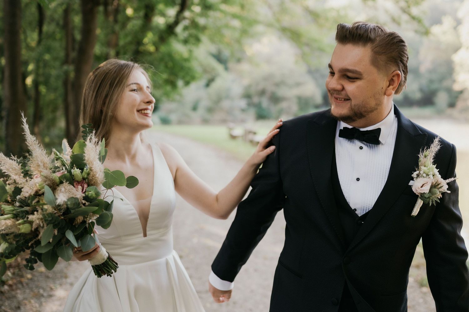 Happy newlyweds share a candid moment while holding a rustic bouquet in a garden setting.