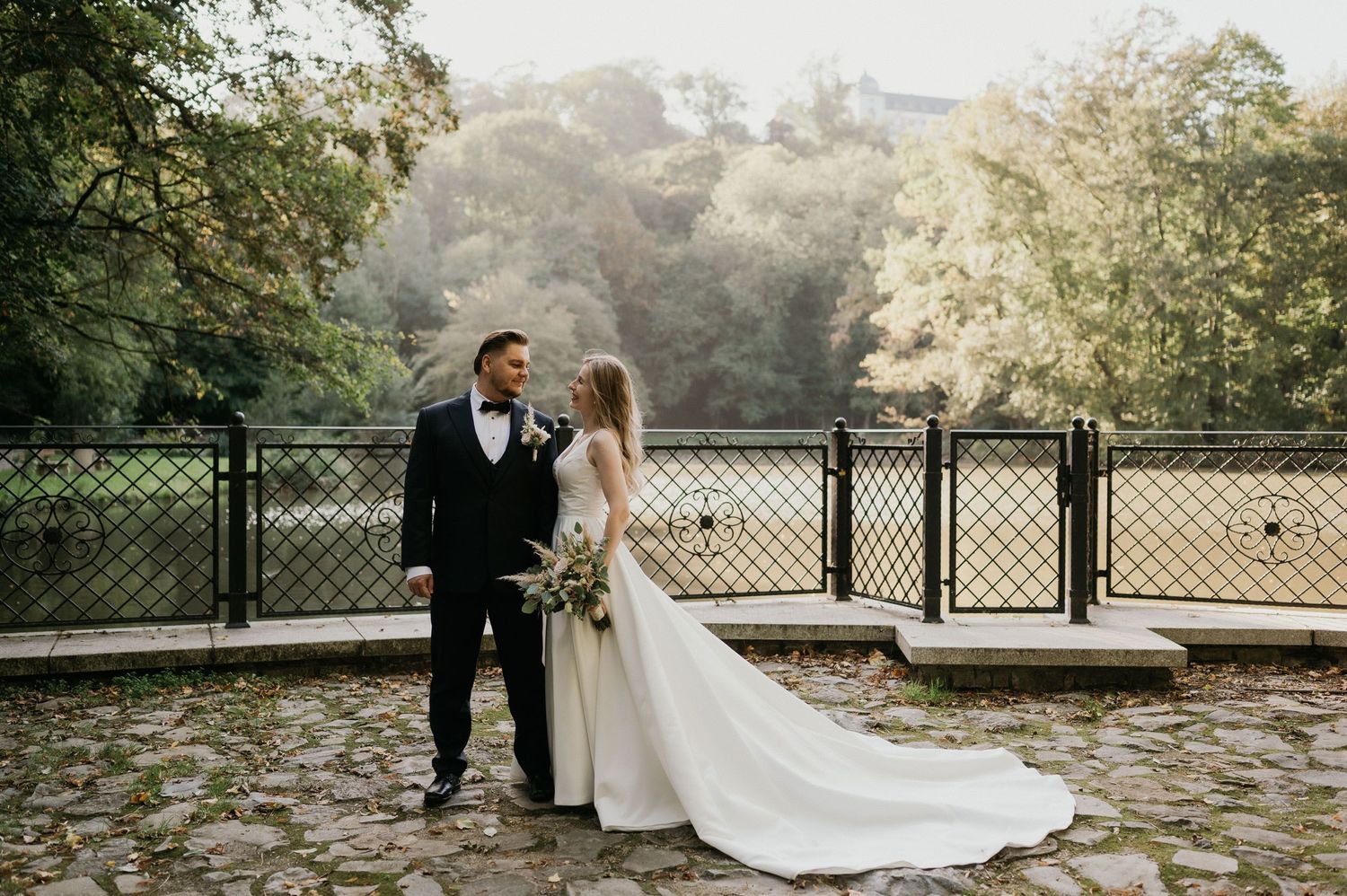 Elegant wedding couple sharing a romantic moment on a rustic bridge surrounded by autumn foliage.