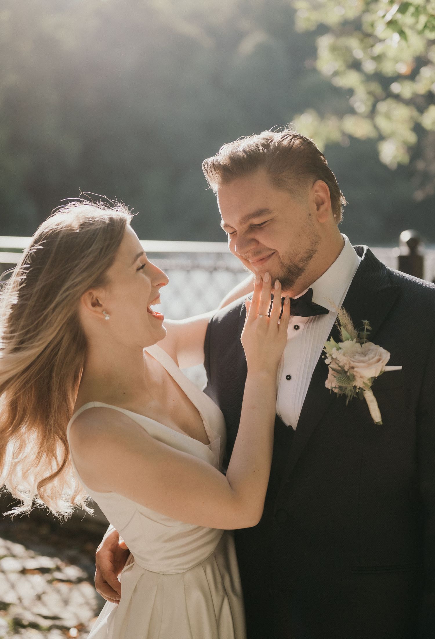 Candid moment of bride caressing groom's face in golden sunlight.
