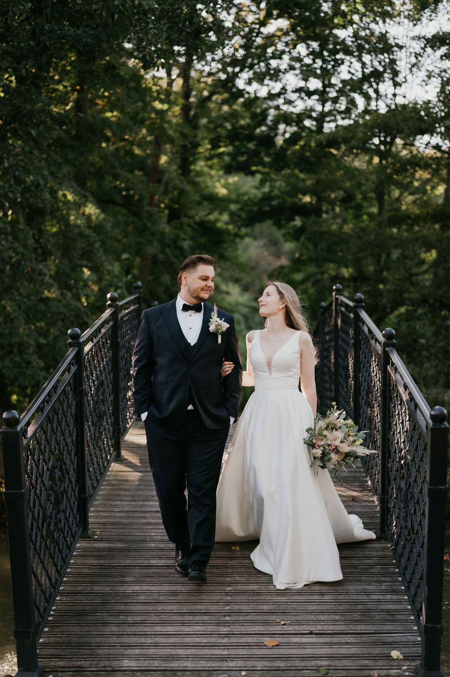 Joyful couple walking together across wooden bridge during wedding photoshoot.