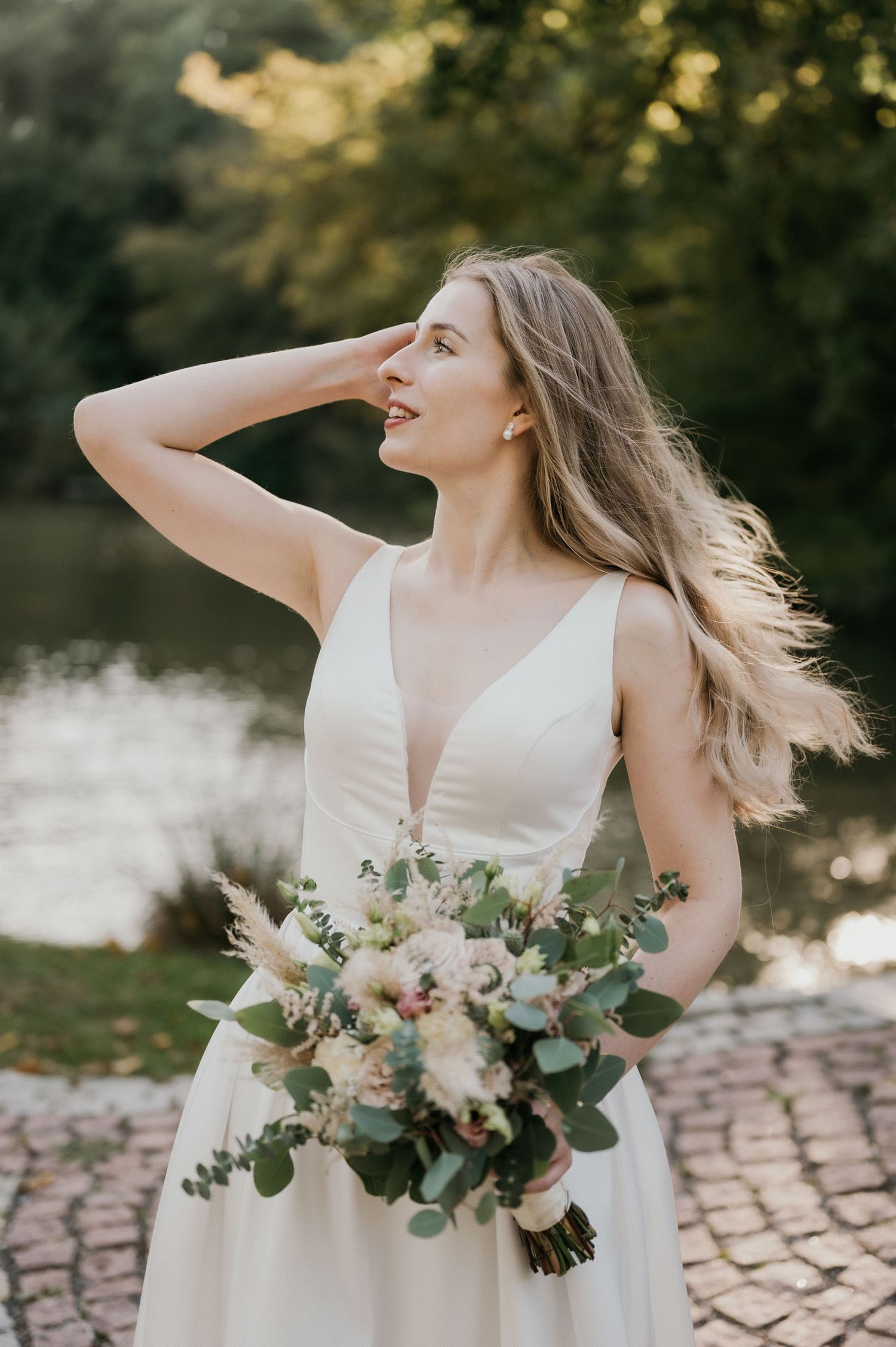 A bride in an elegant white gown laughs while holding a pastel bouquet against a sunset backdrop.
