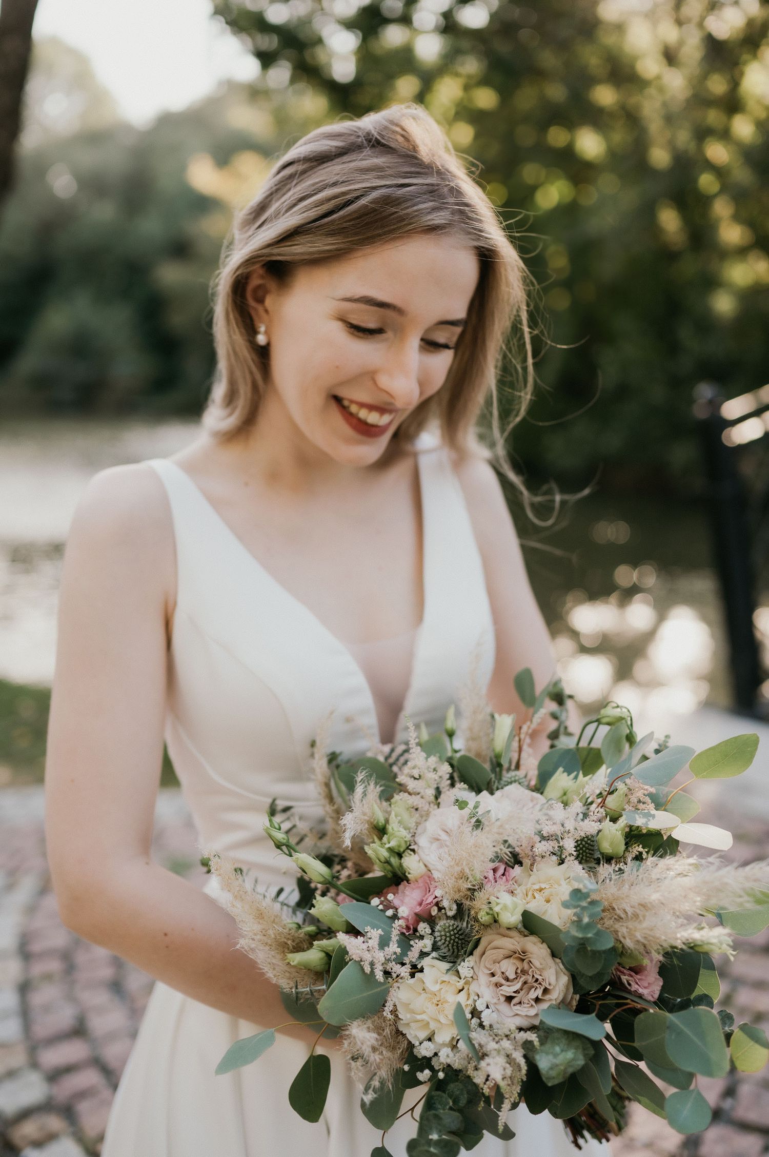 A bride with a natural smile holds a lush bouquet of blush and white flowers with eucalyptus.